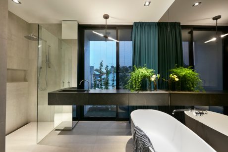 Sleek modern bathroom with dark vanity, curtains, and potted plants overlooking cityscape.
