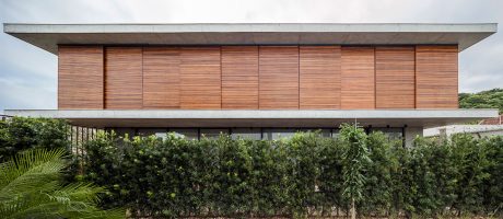 A modern, wood-paneled building with a prominent roofline and lush, tropical vegetation surrounding it.