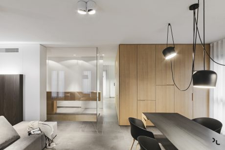 Modern, minimalist apartment featuring sleek wood cabinetry, pendant lights, and glass partition.