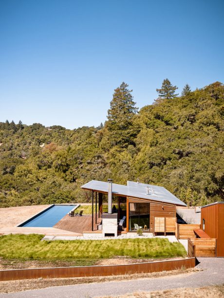 A contemporary wooden cabin nestled in a lush forest, with a sleek pool and deck.