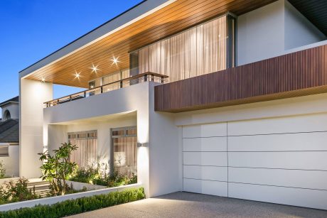 Modern, two-story home with sleek, wood-paneled exterior, large windows, and illuminated balcony.