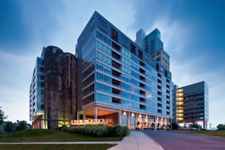 Towering modern architecture with glass facades and illuminated signage against blue sky.