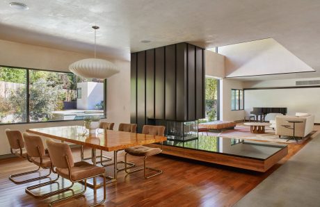 Spacious living room with wooden dining table, glass walls, and modern lighting fixtures.