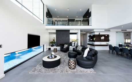 Large open-plan living space with contemporary furniture, high ceilings, and floor-to-ceiling windows overlooking a pool.