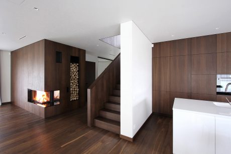 Spacious modern interior with warm wood paneling, a fireplace, and minimalist staircase.
