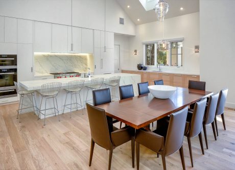 Spacious modern kitchen with marble backsplash, wood dining table, and sleek lighting.