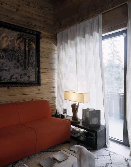 Cozy cabin interior with rustic wooden walls, plush orange sofa, and scenic artwork.