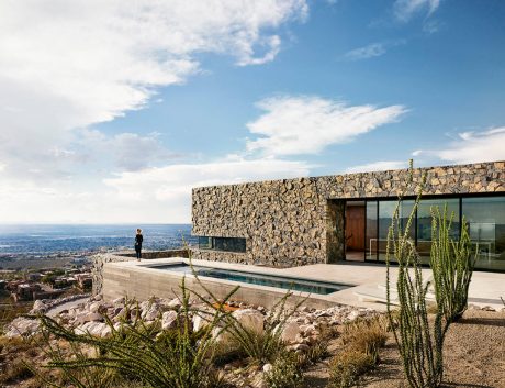 Modern stone exterior with floor-to-ceiling glass walls, pool, and desert landscaping.