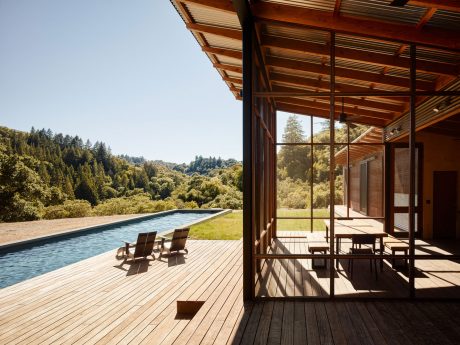 Wooden outdoor deck with pool, surrounded by lush greenery and framed by a wooden pavilion.