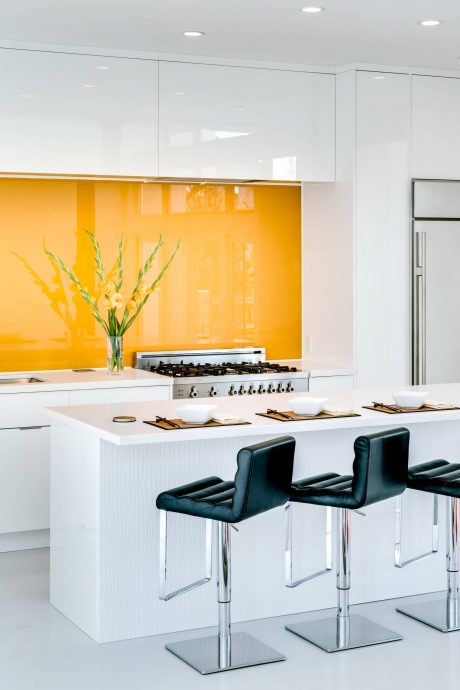 Sleek modern kitchen with white cabinetry, vibrant yellow backsplash, and stylish black bar stools.