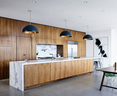 A modern kitchen with wood paneled walls, marble countertops, and black pendant lights.