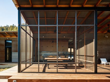Rustic wooden structure with metal framed glass walls opening to a deck and outdoor dining area.