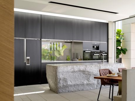 Modern kitchen with sleek black cabinets, integrated appliances, and a large stone island countertop.