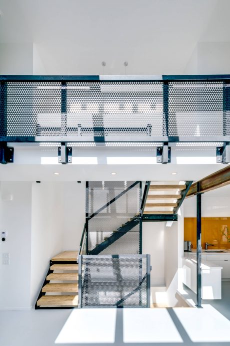 A modern, open-concept interior with a metal mesh balcony and a wooden staircase.