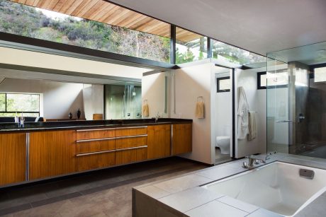 Spacious modern bathroom with glass walls, wood cabinetry, and a sunken bathtub.