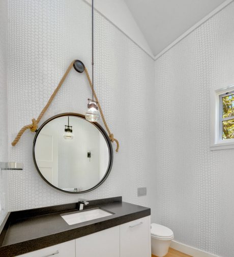 Sleek modern bathroom with hexagonal tile walls, round mirror, and dark countertop.