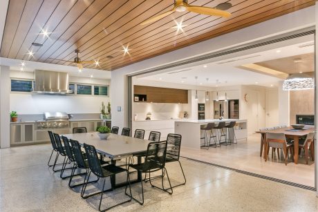 Open-concept kitchen and dining area with modern furnishings, high ceilings, and wood paneling.