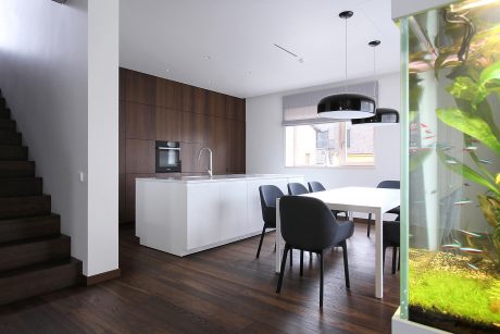 Modern kitchen and dining area with sleek white cabinetry, wood accents, and a large aquarium.