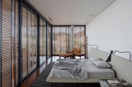Minimalist bedroom with floor-to-ceiling slatted blinds, neutral bedding, and a low wooden platform bed.