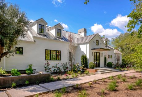 A large, modern farmhouse-style home with a slate roof, dormers, and a covered entry.