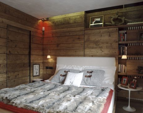 A cozy bedroom with rustic wood paneling, bookshelves, and a plush fur-covered bed.