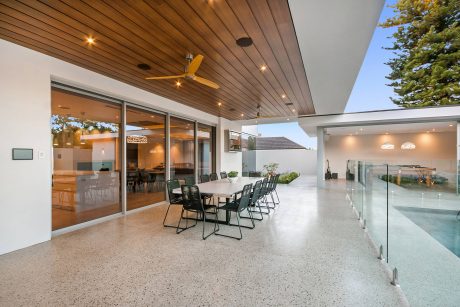 Well-designed outdoor living space with wooden ceiling, ceiling fan, and glass doors leading to interior.
