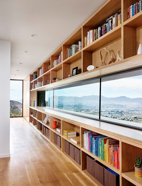 Expansive floor-to-ceiling bookshelves frame panoramic mountain view windows.