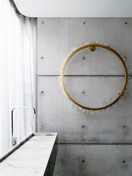 A minimalist bathroom design with a round gold-framed mirror and concrete walls and vanity.
