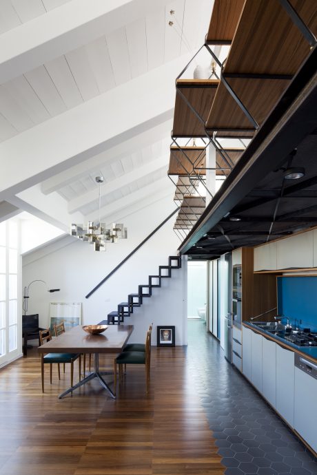 An open concept dining and kitchen area with a modern industrial aesthetic, featuring wooden ceilings, black metal staircase, and hexagonal tile flooring.
