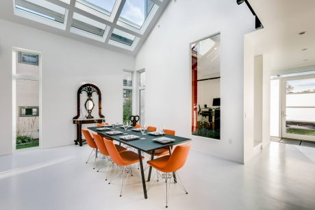 Bright, modern dining room with vaulted skylight, sleek black table, and vibrant orange chairs.