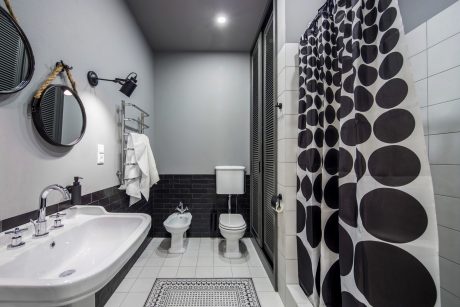 Minimalist bathroom with black and white pebble-patterned curtain, tiled walls, and vanity.