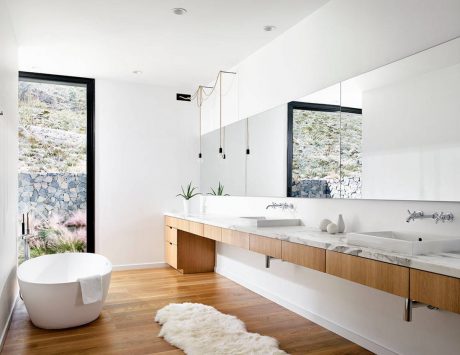 A modern, minimalist bathroom with a freestanding tub, wooden vanity, and floor-to-ceiling windows.