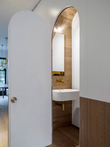 Minimalist bathroom design with curved arch, wood panel accent wall, and pedestal sink.