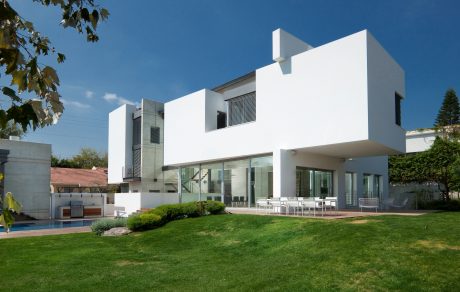 Modern, minimalist architecture with clean lines and large glass windows overlooking a landscaped yard and pool.