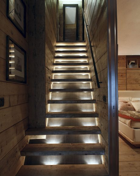 Rustic wooden staircase with recessed lighting, leading to a cozy living space.