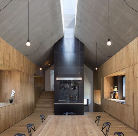 A modern, wood-lined interior with a high ceiling, pendant lights, and a sleek kitchen.