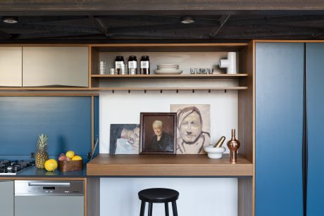 Warm, modern kitchen with wooden shelves, artistic decor, and integrated appliances.