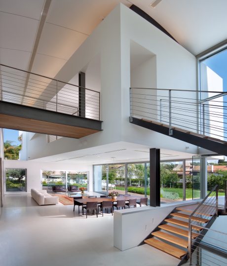 Spacious open-plan interior with wooden stairs, glass walls, and contemporary furnishings.