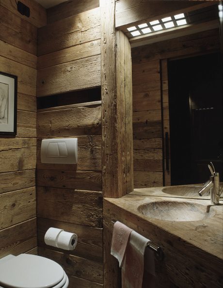 Rustic bathroom with weathered wooden walls, stone sink basin, and minimal fixtures.