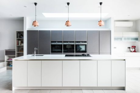 A modern kitchen with minimalist white and gray cabinetry, pendant lights, and built-in appliances.