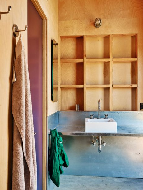 A rustic, wood-paneled bathroom with a metal sink and open shelving, showcasing a minimalist design aesthetic.