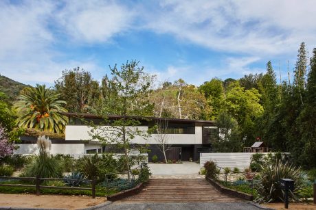 A modern, minimalist residential structure surrounded by lush, verdant vegetation.