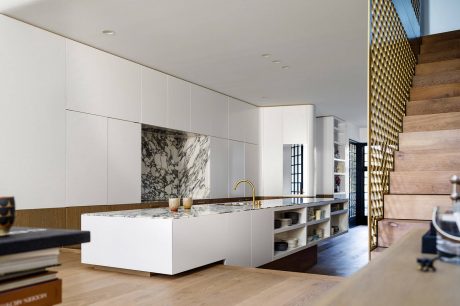 Sleek, modern kitchen with white cabinets, marble countertops, and wood accents. Geometric lighting and shelving add visual interest.