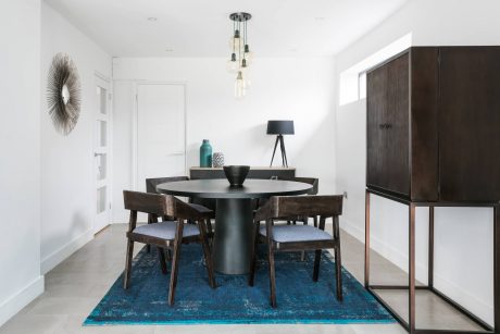 Modern dining room with round dark table, tufted chairs, and statement lighting fixture.
