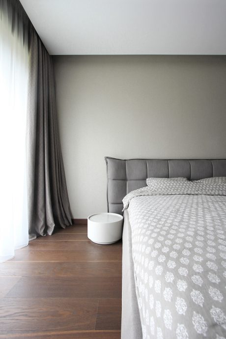A modern bedroom with a gray upholstered headboard, patterned bedding, and minimalist decor.