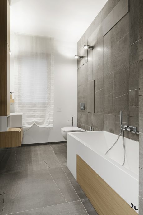 Modern minimalist bathroom with sleek gray tile walls, freestanding tub, and wooden vanity.