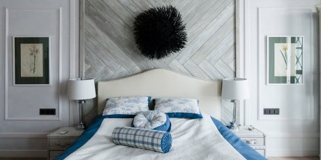 Cozy bedroom with herringbone-patterned wall, plush bedding, and artistic light fixtures.