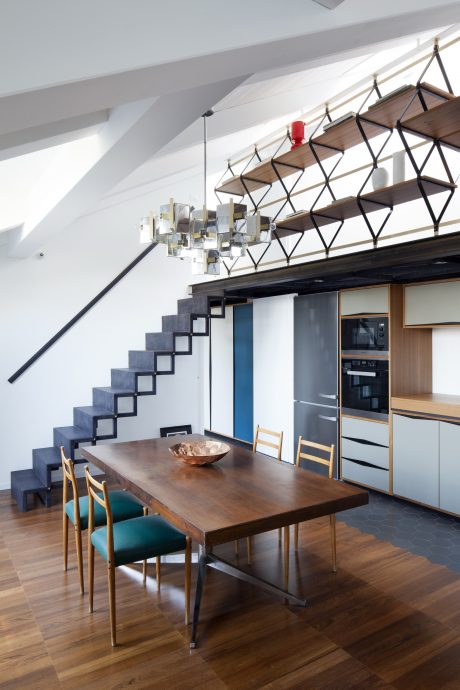 A modern kitchen and dining area with a geometric staircase, shelving, and lighting.