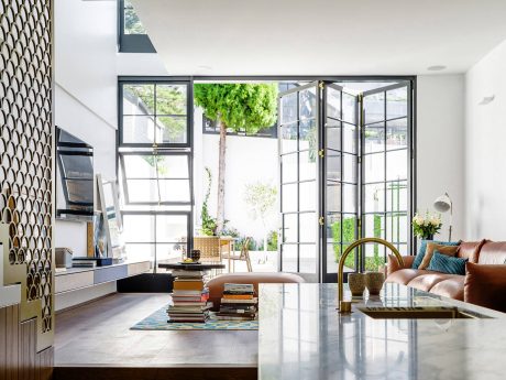 Contemporary living room with large glass doors, natural greenery, and modern furniture.