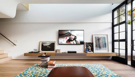 Modern living room with wooden shelving, artwork, and colorful patterned rug.